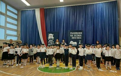 na sali sportowej, na granatowym tle ustawieni pierwszacy wraz z wychowawcami i nauczycielami wspomagającymi