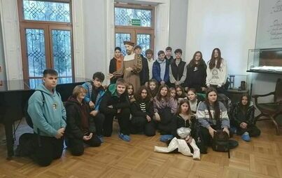 grupa uczestników w sali muzeum, wśród nich stoi postać Jana Kochanowskiego